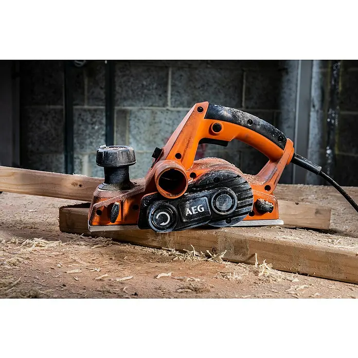 AEG Elektrohobel PL700 700 W - 700 W, Hobeltiefe: 0 mm - 2 mm, Leerlaufdrehzahl: 17.000 U/min - Oranger und schwarzer AEG Elektrohobel, bedeckt mit Holzspänen, auf einem Holzbrett mit weiteren Spänen.