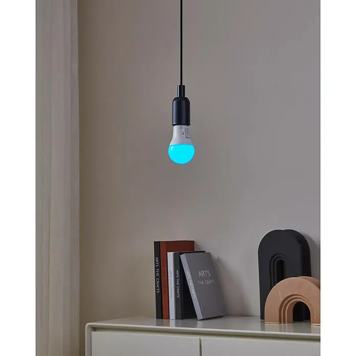 Eglo connect.z Smart-LED-Lampe Zigbee RGB/CCT - E27, Dimmbarkeit: Dimmbar, RGBW, 806 lm, 9 W - Nahaufnahme einer intelligenten LED-Lampe, die an einer Schnur hängt und neben Dekorationsbüchern und Ornamenten auf einem Sideboard steht.