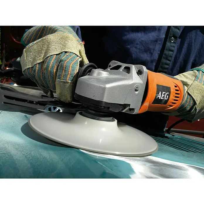 AEG Tellerschleifer SE 12-180 - 1.200 W, Durchmesser Schleifteller: 180 mm, Leerlaufdrehzahl: 1.800 U/min - 1.400 U/min - Person mit Handschuhen nutzt orangen und grauen Winkelschleifer mit Polierpad auf türkiser Oberfläche.