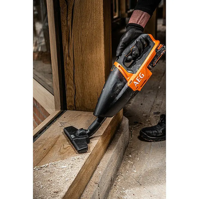 AEG Akku-Handstaubsauger BHSS18C-0 - Ohne Akku, Behältervolumen: 860 l - Eine Person nutzt einen orange-schwarzen AEG Handstaubsauger, um Sägemehl von einem Holzfensterrahmen zu entfernen.