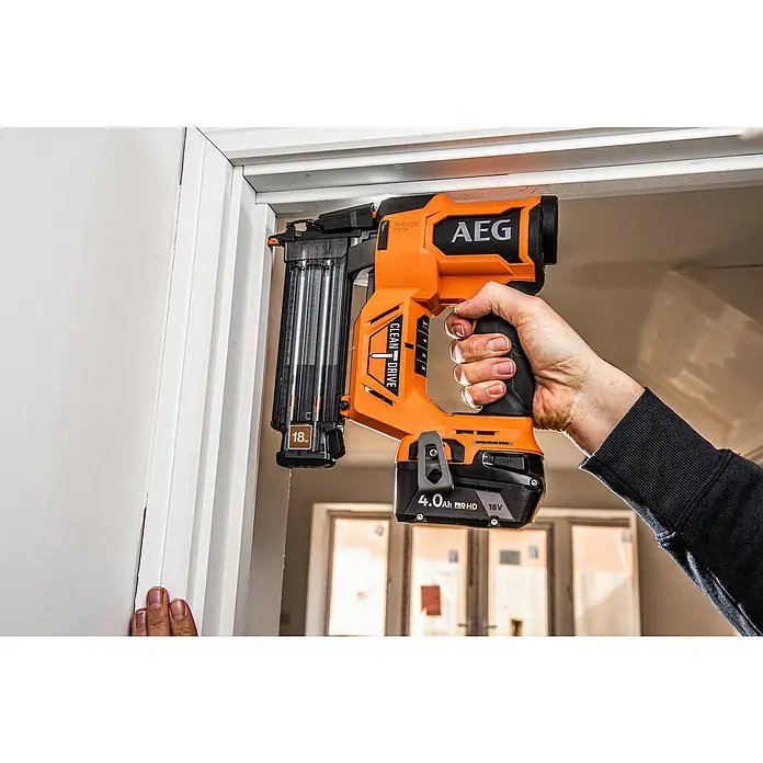 AEG Pro 18V Akku-Nagler B18BN18-0 - 18 V, Ohne Akku, Länge Nagel: 16 mm - 54 mm - Eine orange-schwarze AEG 18V Stiftnagler wird von einer Hand gehalten und verwendet, um eine weiße Zierleiste an einem Türrahmen zu befestigen.
