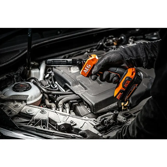AEG Pro 18V LED-Akkustrahler BSL 18 - 18 V, Ohne Akku, 800 lm - Mechanikerhand hält orange-schwarze AEG Arbeitsleuchte, die einen Motorraum beleuchtet.