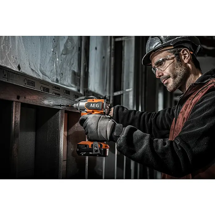 AEG Pro 18V Akku-Schlagschrauber Kompakt BSS 18C3B3 - 18 V, Ohne Akku, 350 Nm - Mann mit orange-schwarzem AEG Schlagschrauber befestigt Schraube in Metallrahmen, trägt Schutzbrille und Helm.