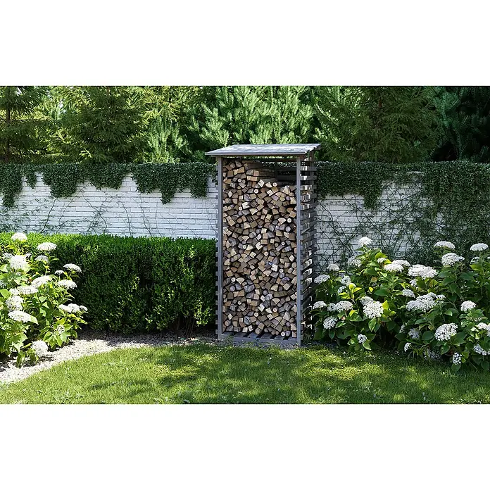 Joda Kaminholzregal - 100 x 100 x 201 cm, Holz, Grau - Ein Holzregal, gefüllt mit geschnittenem Brennholz, steht in einem gepflegten Garten mit Blumen und Sträuchern. Das Holz ist sauber gestapelt.