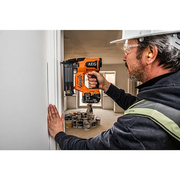 AEG Pro 18V Akku-Nagler B18BN18-0 - 18 V, Ohne Akku, Länge Nagel: 16 mm - 54 mm - Ein orange-schwarzer AEG Nagler wird von einer Person gehalten, die Leisten an einer weißen Wand befestigt.