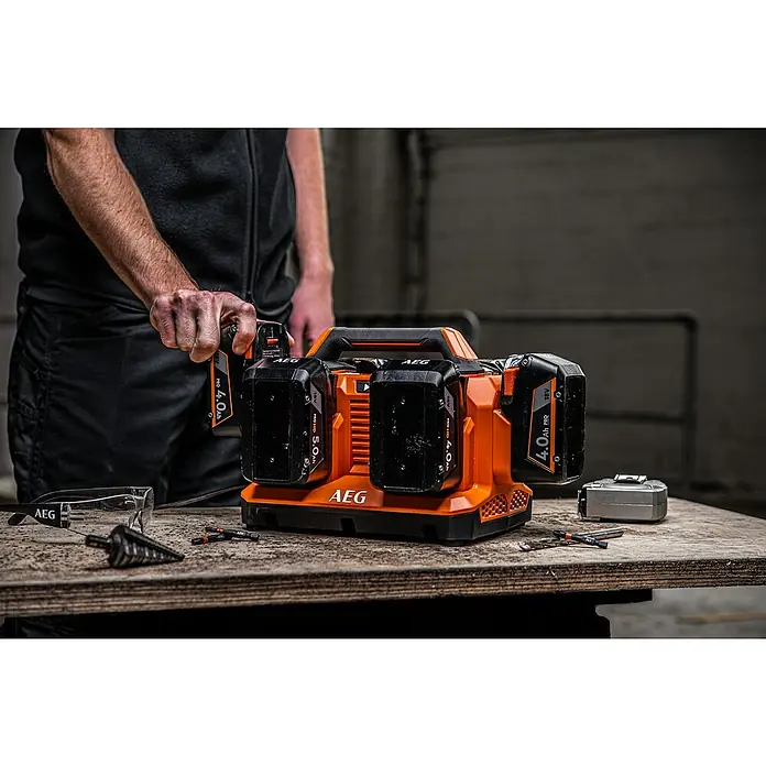 AEG Pro 18V Batterie-Ladegerät BL18C6 - 18 V, Ohne Akku, Ladestrom: 4 A - Mann steckt einen orangen AEG 18V Akku in ein Mehrfachladegerät auf einer Werkbank mit Werkzeugen.