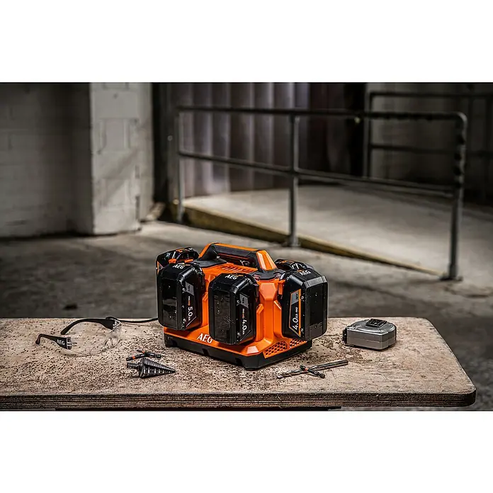 AEG Pro 18V Batterie-Ladegerät BL18C6 - 18 V, Ohne Akku, Ladestrom: 4 A - Oranges und schwarzes AEG Mehrfach-Akku-Ladegerät mit vier Akkus auf Holzuntergrund, umgeben von Werkzeugen.