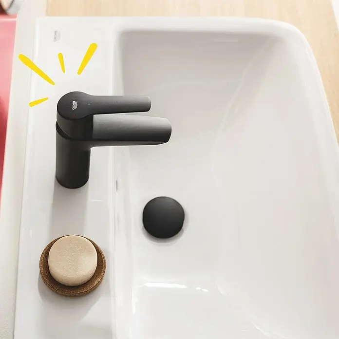 Grohe Start Waschtischarmatur S-Size - Ausladung Armatur: 109 mm, Matt, Schwarz - Nahaufnahme eines weißen Waschbeckens mit einer modernen, mattschwarzen Armatur und einem minimalistischen Seifenhalter.