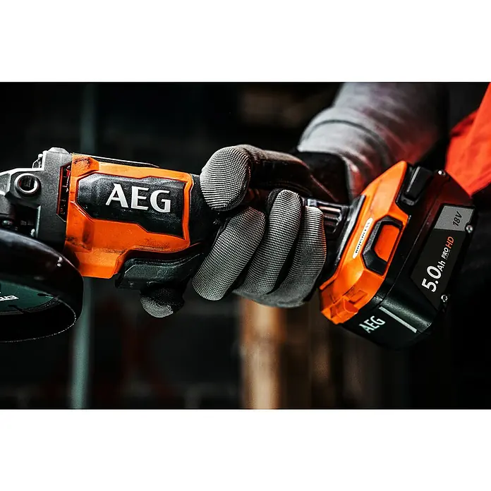 AEG Pro 18V Akku-Winkelschleifer BEWS 18-125BLPX2 - 18 V, Ohne Akku, Durchmesser Scheibe: 125 mm - Behandschuhte Hand hält einen orange-schwarzen AEG Akku-Winkelschleifer mit einem 18V 5.0Ah Akku.