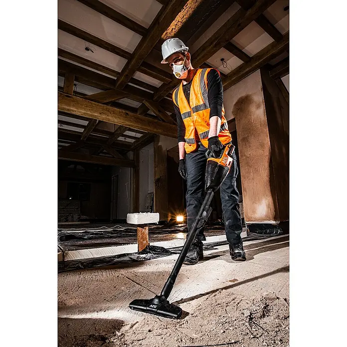 AEG Akku-Handstaubsauger BHSS18C-0 - Ohne Akku, Behältervolumen: 860 l - Arbeiter reinigt staubigen Baustellenboden mit orange-schwarzem AEG Akku-Staubsauger.