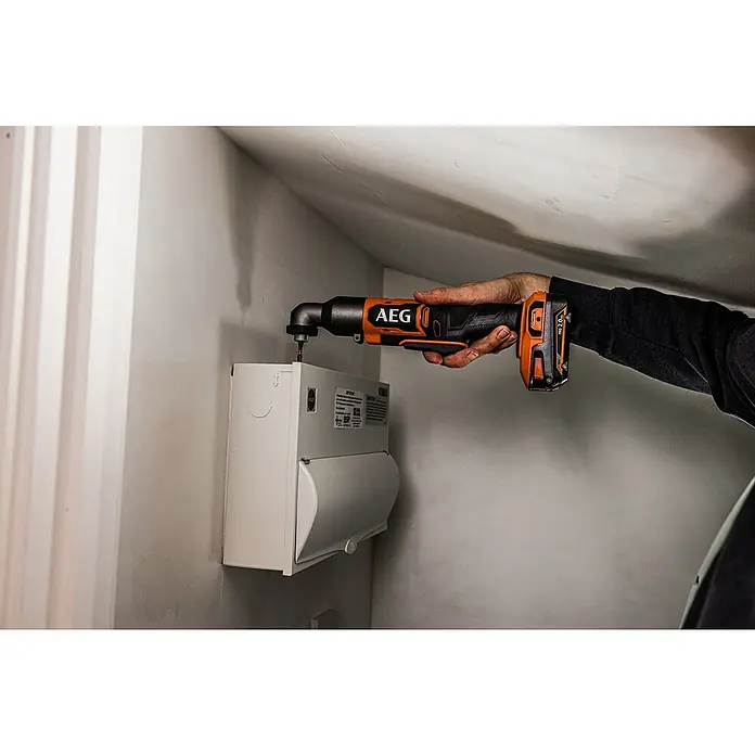 AEG Pro 18V Akku-Winkelbohrschrauber BSS 18SRABL - 18 V, Ohne Akku, 150 Nm - Eine Person benutzt einen orange-schwarzen AEG Winkelbohrschrauber, um in einen weißen Stromkasten an der Wand zu schrauben.