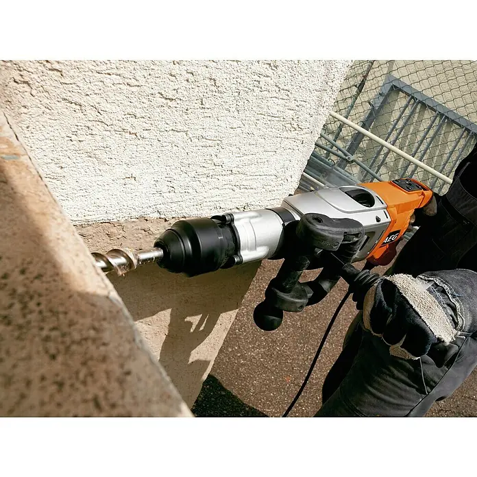 AEG Kombihammer PN 11E - 1.700 W, 20 J, SDS-Max-Aufnahme - Orange-silberner AEG Bohrhammer bohrt in eine texturierte Betonwand, gehalten von einer Person in Arbeitshandschuhen.