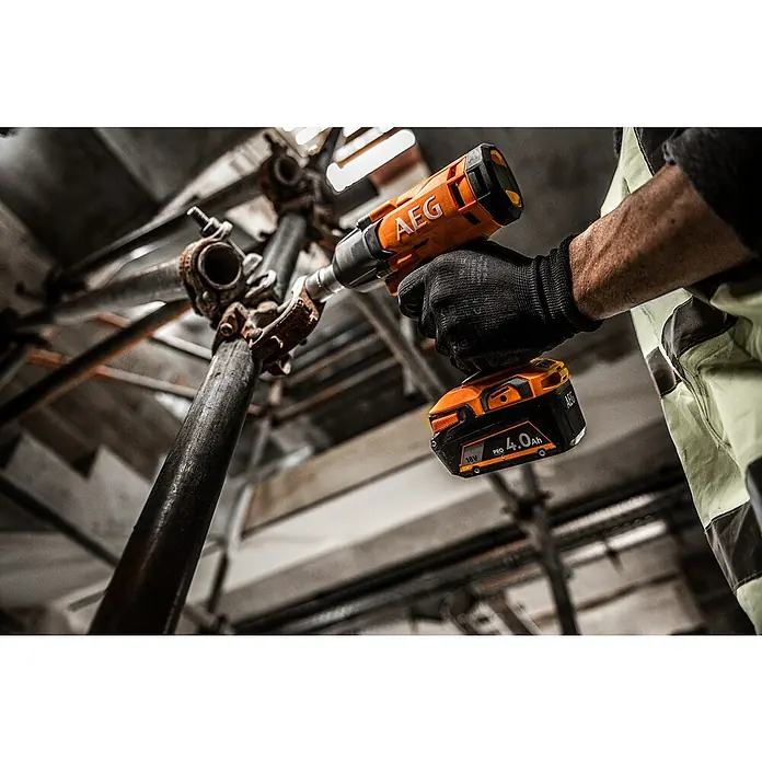 AEG Pro 18V Akku-Schlagschrauber BSS 18C12ZC - 18 V, Ohne Akku, 439 Nm - Eine behandschuhte Hand hält eine orange-schwarze AEG Akkubohrmaschine mit 18V 4.0Ah Akku, verwendet an rostigem Metallgerüst.