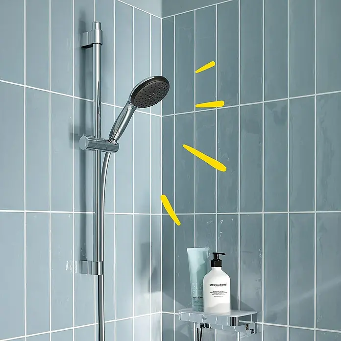 Grohe Vitalio Start Brausegarnitur 110 1 - Lochabstand: 47 cm - 62 cm, Chrom, Kunststoff - Nahaufnahme einer modernen Dusche mit Duschkopf, Shampoo und Duschgel auf einem Regal, hervorgehoben durch gelbe Strahlen.