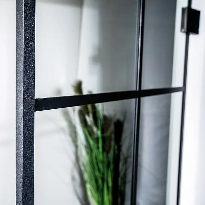 Room Plaza Slimwork Drehtür-Komplettset Typ 8 - 959 x 1.972 mm, DIN Anschlag: Links, Klarglas - Nahaufnahme eines schwarz strukturierten Metallrahmens mit Glasscheiben, Teil einer modernen Raumtrennwand oder Tür.