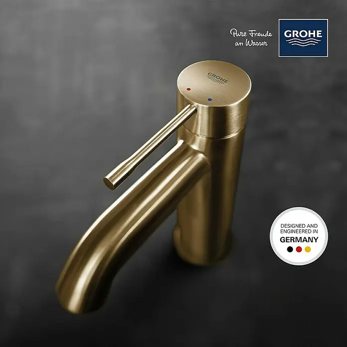 Grohe Essence New Waschtischarmatur S-Size - Ohne Zugstange, Cool Sunrise, Matt - Nahaufnahme eines goldenen Grohe Wasserhahns mit deutscher Kennzeichnung für Design und Technik.
