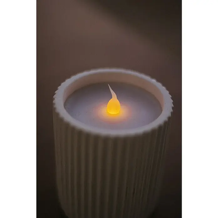 New Garden Vela LED para exteriores Dolo - 10 cm, Blanco - Primer plano de una vela LED con luz amarilla cálida en un candelabro blanco acanalado, creando un ambiente acogedor.