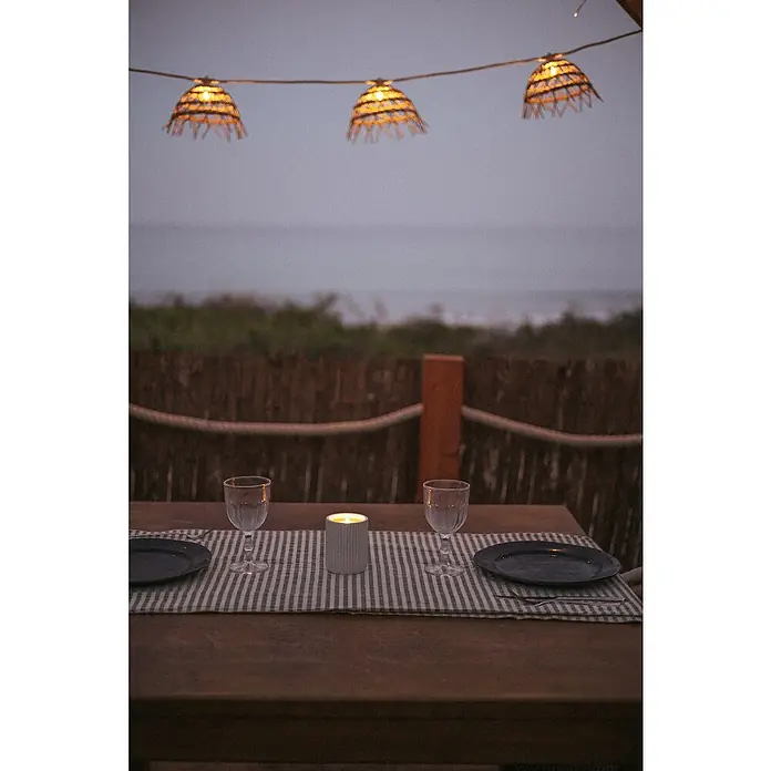 New Garden Lámpara decorativa solar y barra decorativa Alma - Marrón, Redonda, 10 ud. - Mesa ambientada con vela, vajilla e iluminación decorativa para una cena romántica junto al mar.