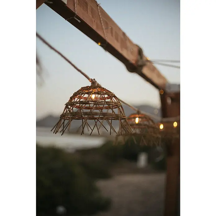 New Garden Lámpara decorativa solar y barra decorativa Alma - Marrón, Redonda, 10 ud. - Primer plano de una lámpara decorativa de mimbre colgando de un marco de madera, creando un ambiente cálido y acogedor.