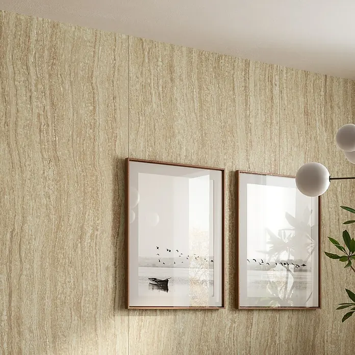 Corso Italia Feinsteinzeugfliese Traventino - 120 x 278 cm, Sand, Matt - Hellbraune, linear gemusterte Wandpaneele, verziert mit gerahmten Bildern und einer Pflanze.