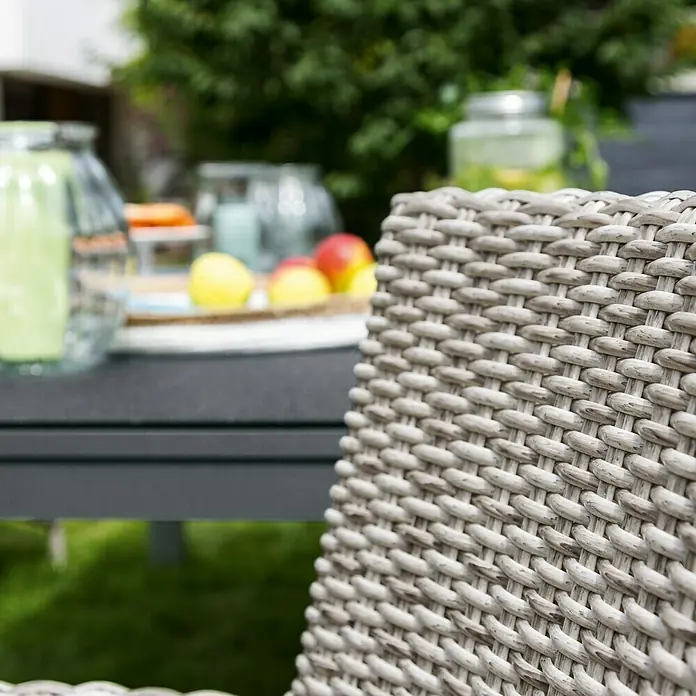 Sunfun Maja Mesa de jardín XL - L x An x Al: 280 x 100 x 75 cm, Aluminio, vidrio, Rectangular, Antracita, Extensible - Primer plano de una silla de jardín de ratán gris con una mesa y vasos al fondo.