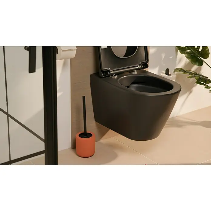 Wenko WC-Bürstengarnitur Avellino - Keramik, Terracotta - Nahaufnahme einer modernen, mattschwarzen Wandtoilette mit offenem Deckel, neben einer orangefarbenen Toilettenbürste in einem stilvollen Badezimmer.