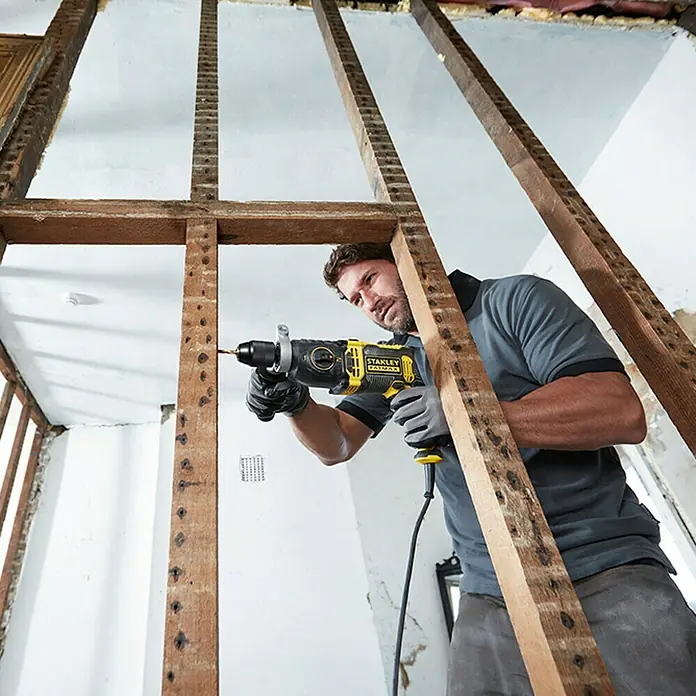 Stanley FatMax Taladro percutor FMEH1100K con maletín - 1.100 W, Portabrocas de sujeción rápida - Un artesano utiliza un taladro Stanley Fatmax en una habitación sin terminar.