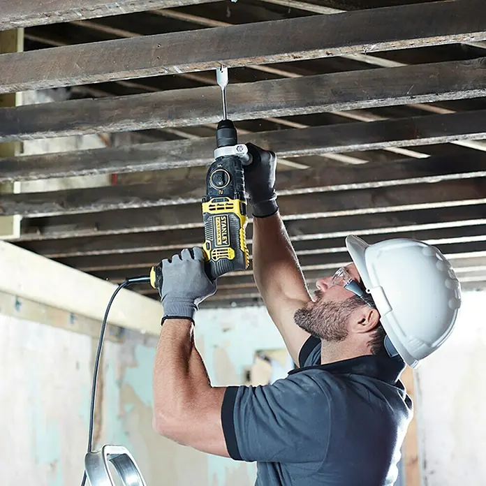 Stanley FatMax Taladro percutor FMEH1100K con maletín - 1.100 W, Portabrocas de sujeción rápida - Un artesano perfora un techo con un taladro Stanley amarillo y negro. El trabajador lleva casco por seguridad.