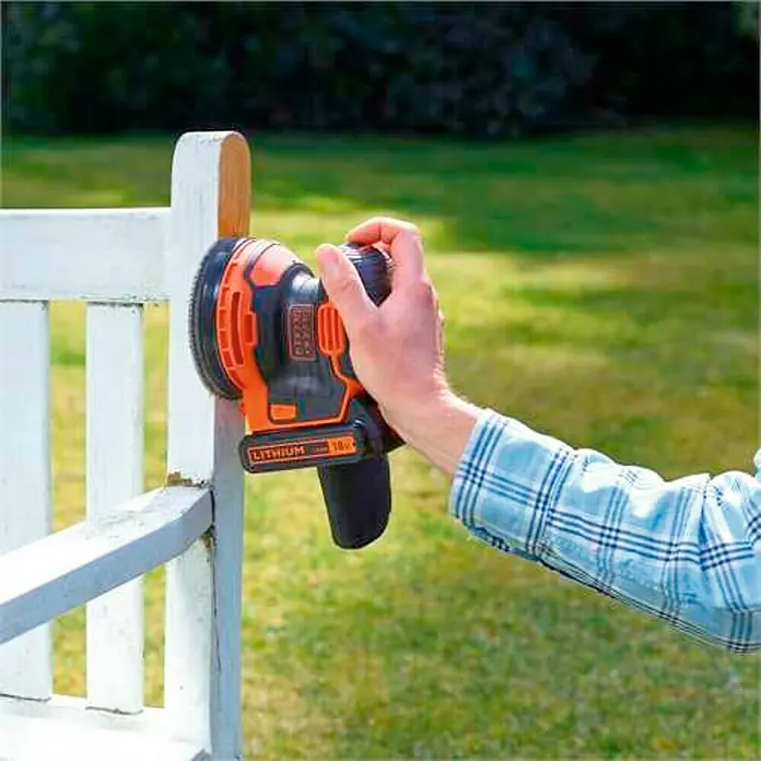 Black+Decker 18V PowerConnect Lijadora excéntrica de batería BDCROS18-QW - 18 V, Iones de litio, 1,5 Ah, 1 batería, 125 mm - Un hombre usa una lijadora orbital aleatoria inalámbrica Black+Decker para lijar una cerca de madera blanca al aire libre.