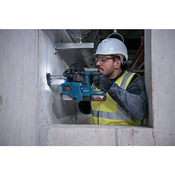 Bosch Professional AMPShare 18V Akku-Bohrhammer PRO GBH 18V-22 - 18 V, 2 Akkus, 4 Ah, 1,9 J - Ein Bauarbeiter bohrt mit einem Bosch Akku-Bohrhammer GBH 18V-26 in eine Betonwand. Er trägt Schutzkleidung und einen Helm für die Arbeitssicherheit.
