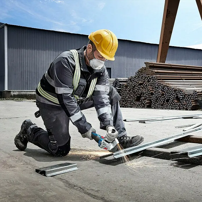 Bosch Professional AMPShare 18V Juego de máquinas - 18 V, 2 baterías, 2 Ah - 4 Ah, 7 pzs. - Un trabajador de la construcción está arrodillado cortando metal con una amoladora angular Bosch, saltan chispas.