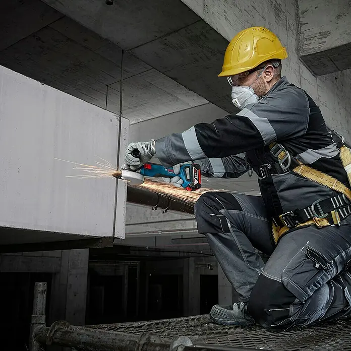 Bosch Professional AMPShare 18V Maschinen-Set 3-Tool-Kit - 18 V, 2 Akkus, 2 Ah - 4 Ah, 7 -tlg. - Ein Bauarbeiter verwendet einen Bosch Akku-Winkelschleifer, um Metall zu schneiden, wobei Funken fliegen und die robuste Bauweise des Werkzeugs betont wird.