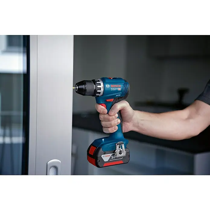Bosch Professional AMPShare 18V Akku-Bohrschrauber GSR 18V-45 PRO 2X2,0AH - 18 V, 2 Akkus, 45 Nm, L-Boxx, 2 Akkus - Ein blauer Bosch Professional Akku-Bohrschrauber mit eingesetztem Bit wird von einer Hand gehalten. Im Hintergrund ist eine Tür zu sehen.
