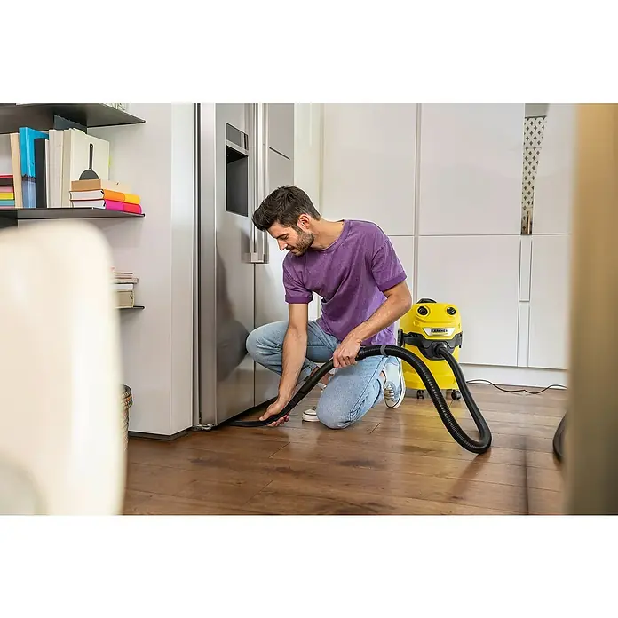 Kärcher Fugendüse flexibel - Passend für: Kärcher Home&Garden Nass/Trockensauger, Kunststoff, 615 mm - Ein Mann kniet und saugt mit einem gelben Kärcher Staubsauger den Boden unter einem Kühlschrank. Das Gerät steht bereit für die Reinigung.