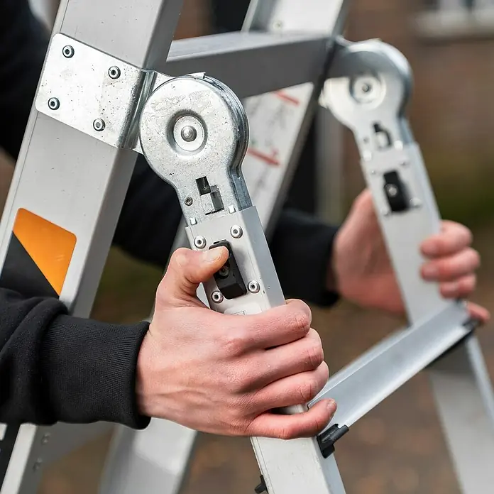Batavia Mehrzweckleiter - Anzahl Tritte: 9 Stk. - Nahaufnahme einer Person, die eine Mehrzweckleiter bedient, wobei der Fokus auf den Verriegelungsmechanismen und der Aluminiumkonstruktion liegt.