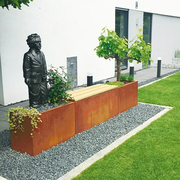 Palatino Exclusive Line Pflanzkasten Lotte - 100 x 40 x 50 cm, Cortenstahl, Rotbraun - Gartenszene mit Rostfarbenem Pflanzkasten mit Holzbänken, Statue und Grünpflanzen, umgeben von Kies und Rasenflächen.