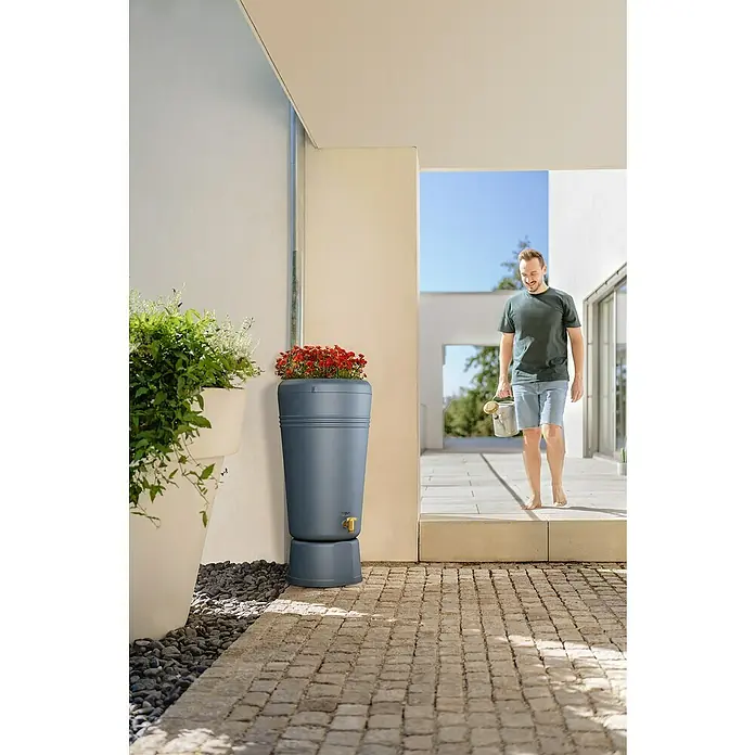 4rain Regenspeicher Azura - 120 l, Graphitgrau - Ein Regenfass in modernem Design mit integriertem Pflanzgefäß und einem Mann, der mit einer Gießkanne in der Hand auf eine Terrasse tritt.