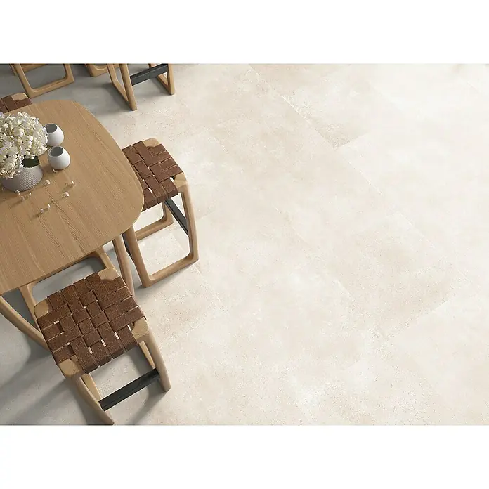 Halcón Pavimento porcelánico Amira - 60,5 x 60,5 cm, Beige, Mate - Vista superior de una mesa de comedor de madera con sillas y decoración sobre un suelo de baldosas claras.