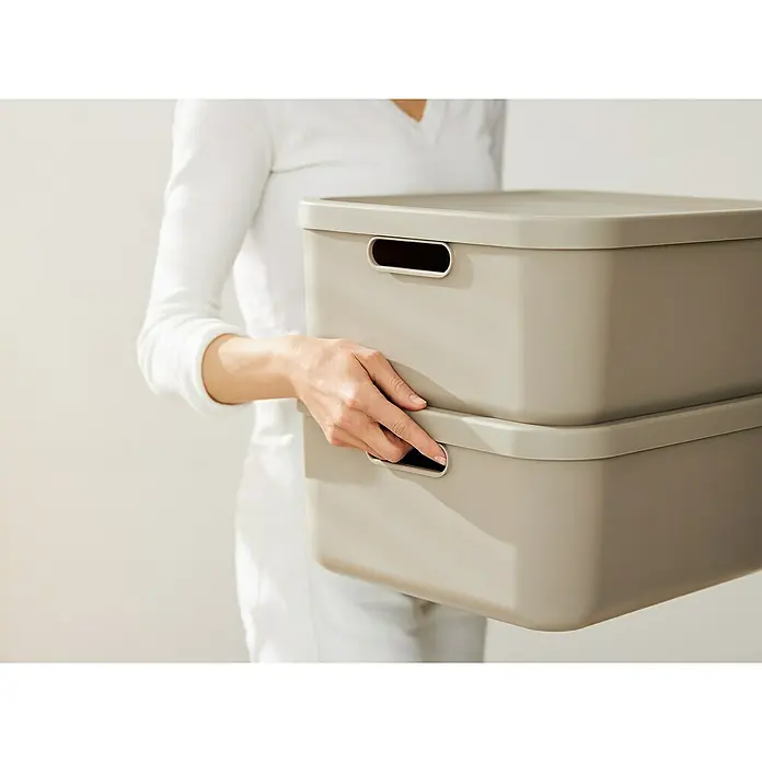 Rotho Aufbewahrungsbox - L x B x H: 39,2 x 35,5 x 17,7 cm, Kunststoff, Cappuccino, 20 l - Eine Person trägt zwei graue Aufbewahrungsboxen mit Griffen. Praktische Aufbewahrungslösung für ein ordentliches Zuhause.