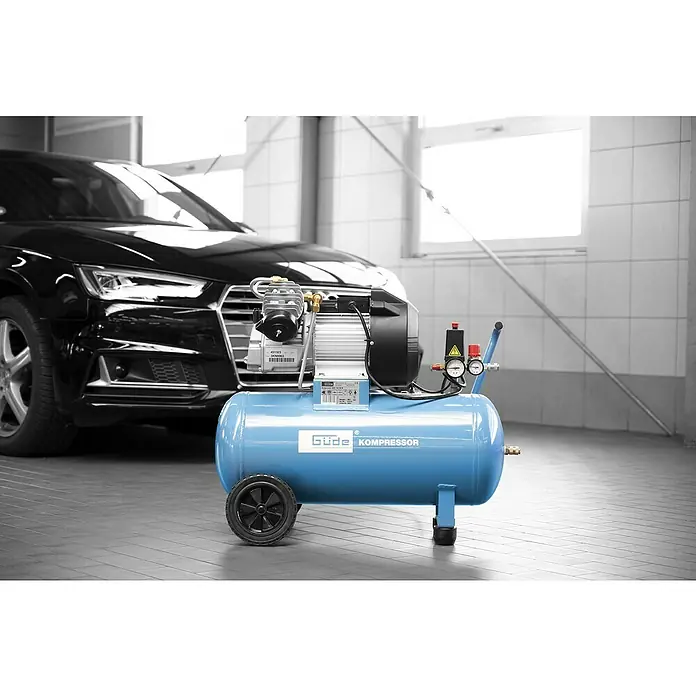 Güde Kompressor 400/10/50 N - 2.200 W, Max. Druck: 10 bar, 10 l, Schmierung: Ölgeschmiert - Blauer Luftkompressor mit schwarzen Rädern und Manometern vor einem schwarzen Auto.