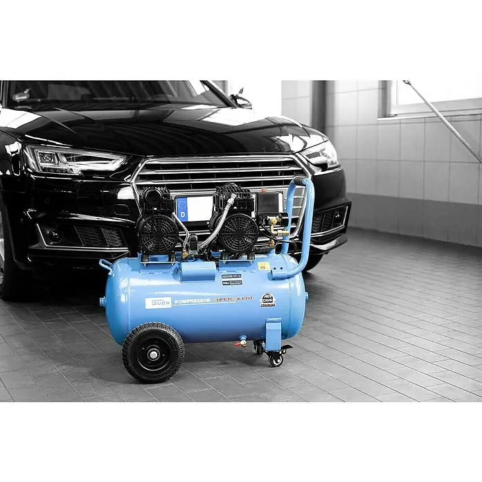 Güde Flüsterkompressor Airpower 275/8/50 Silent - 1.500 W, Max. Druck: 8 bar, 50 l, Schmierung: Ohne - Blauer, fahrbarer Luftkompressor in einer Werkstatt, vor einem schwarzen Auto platziert.