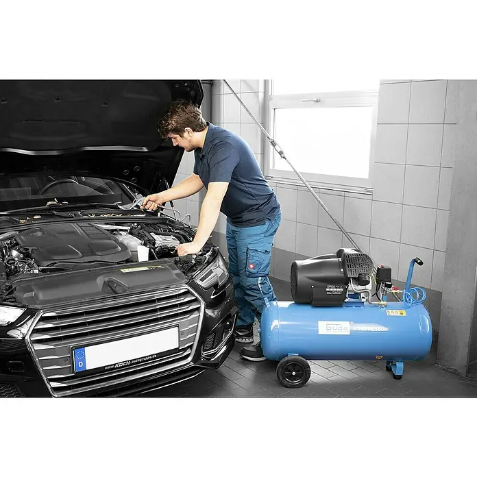 Güde Kompressor 412/8/100 - 2.200 W, Max. Druck: 8 bar, 100 l, Schmierung: Ölgeschmiert - Blauer und schwarzer Kompressor in einer Werkstatt, von einem Mechaniker zur Motorreinigung eines Autos verwendet. Mit Rädern für Mobilität.