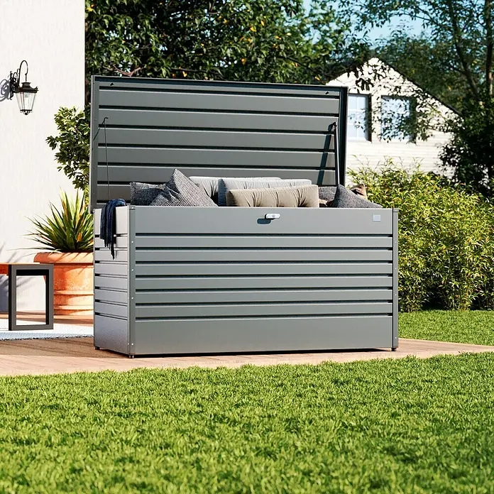 Biohort FreizeitBox Gartenbox FreizeitBox 160 - L x B x H: 160 x 79 x 83 cm, Quarzgrau, Stahl - Dunkelgraue Metall-Gartenbox mit geöffnetem Deckel, gefüllt mit Kissen und Decken, auf Holzterrasse im Garten.