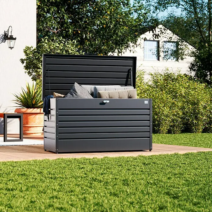 Biohort FreizeitBox Gartenbox FreizeitBox 130 - L x B x H: 134 x 62 x 71 cm, Dunkelgrau Metallic, Stahl - Eine geöffnete, schwarze Gartenbox auf einer Holzterrasse mit Kissen und Decken gefüllt. Ideal zur Aufbewahrung im Aussenbereich.