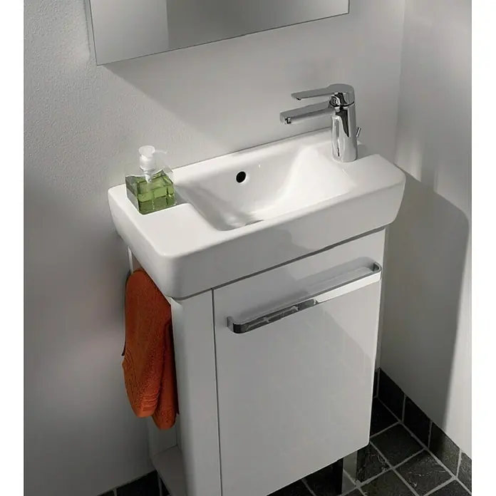 Geberit Renova Comprimo Waschbecken - 50 x 25 cm, Ohne Spezialglasur, Hahnloch: Rechts, Mit Überlauf, Weiß - Nahaufnahme eines modernen weißen Waschbeckenunterschranks mit Armatur, Seifenspender und orangefarbenem Handtuch an der Seite.