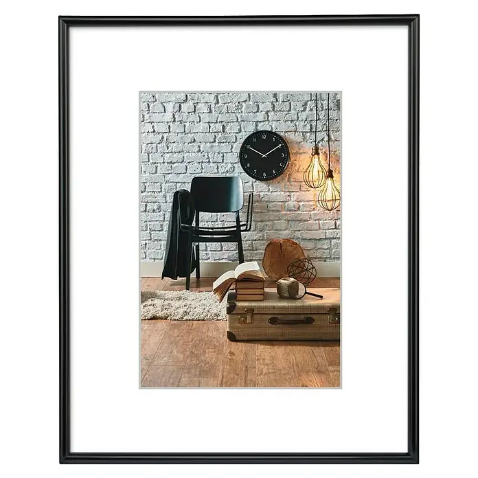 Hama Kunststoffrahmen Sevilla - 50 x 70 cm, Schwarz - Schwarz gerahmtes Bild mit weißem Passepartout, das eine moderne Innenszene mit Stuhl, Uhr und Deko-Leuchten zeigt.