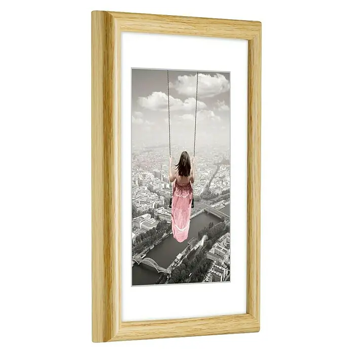 Hama Kunststoffrahmen Swing - 40 x 50 cm, Natur - Heller Holzmaserungsrahmen mit einem Bild eines Mädchens auf einer Schaukel über einer Stadt.