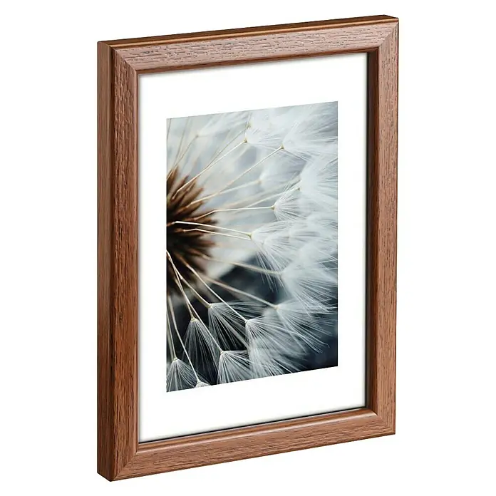 Hama Kunststoffrahmen Breeze - 13 x 18 cm, Nussbaum - Brauner Holzbilderrahmen mit weißem Passepartout und Nahaufnahme eines Pusteblumensamenkopfes.