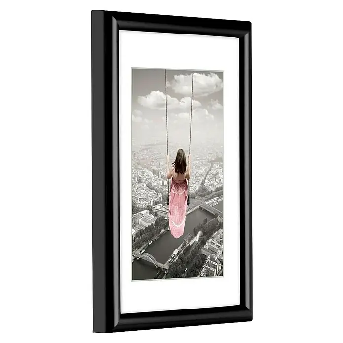 Hama Kunststoffrahmen Swing - 20 x 30 cm, Schwarz - Schwarzer Bilderrahmen mit weißem Passepartout, zeigt Frau in rosa Kleid auf Schaukel über schwarz-weißer Stadt.