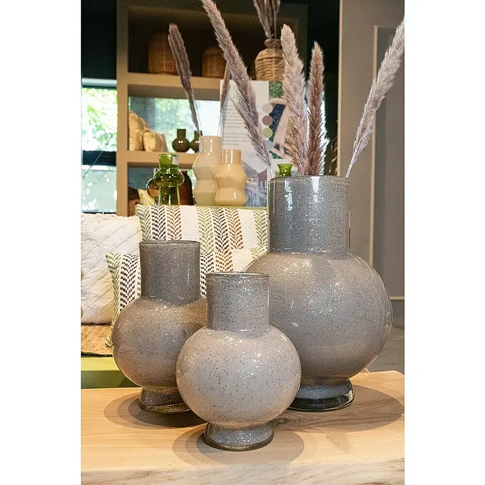 Vase Deborah - Ø x H: 17,5 x 22 cm, Glas, Taupe - Drei graue Vasen unterschiedlicher Größe stehen auf einem Tisch, wobei die größte mit dekorativem Gras gefüllt ist.